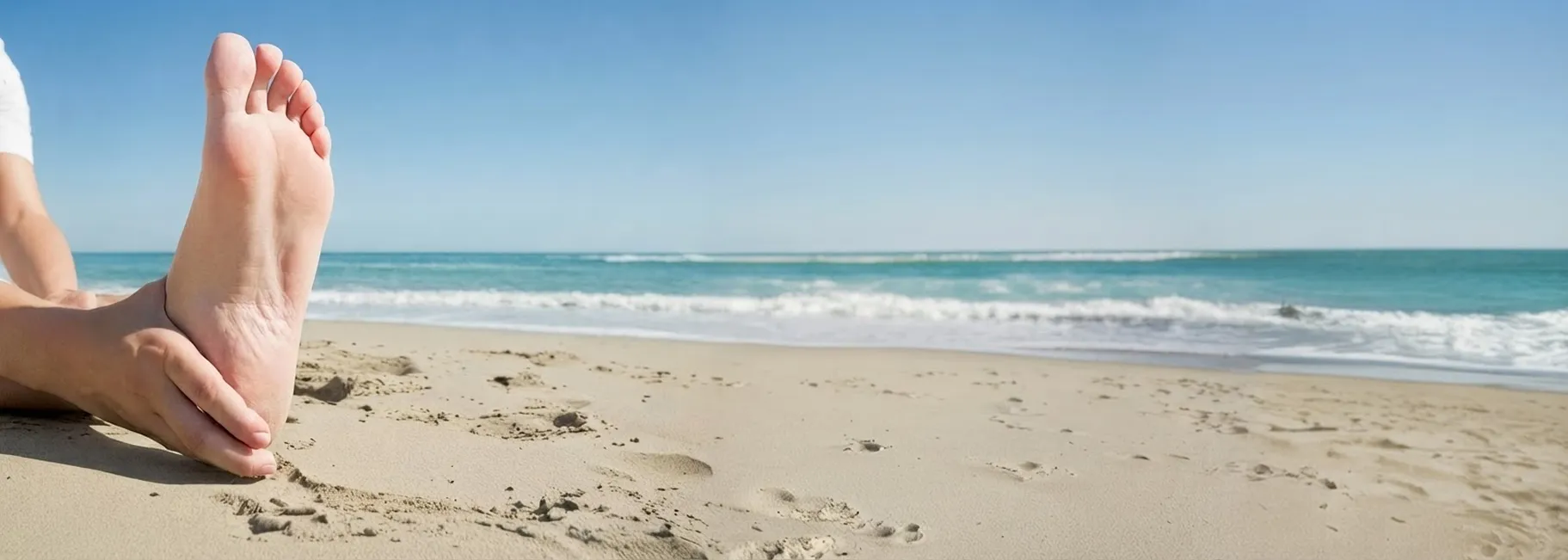 Bild eines Sandstrandes, an dem sich eine Person dehnt. Im Hintergrund ist das Meer zu sehen.